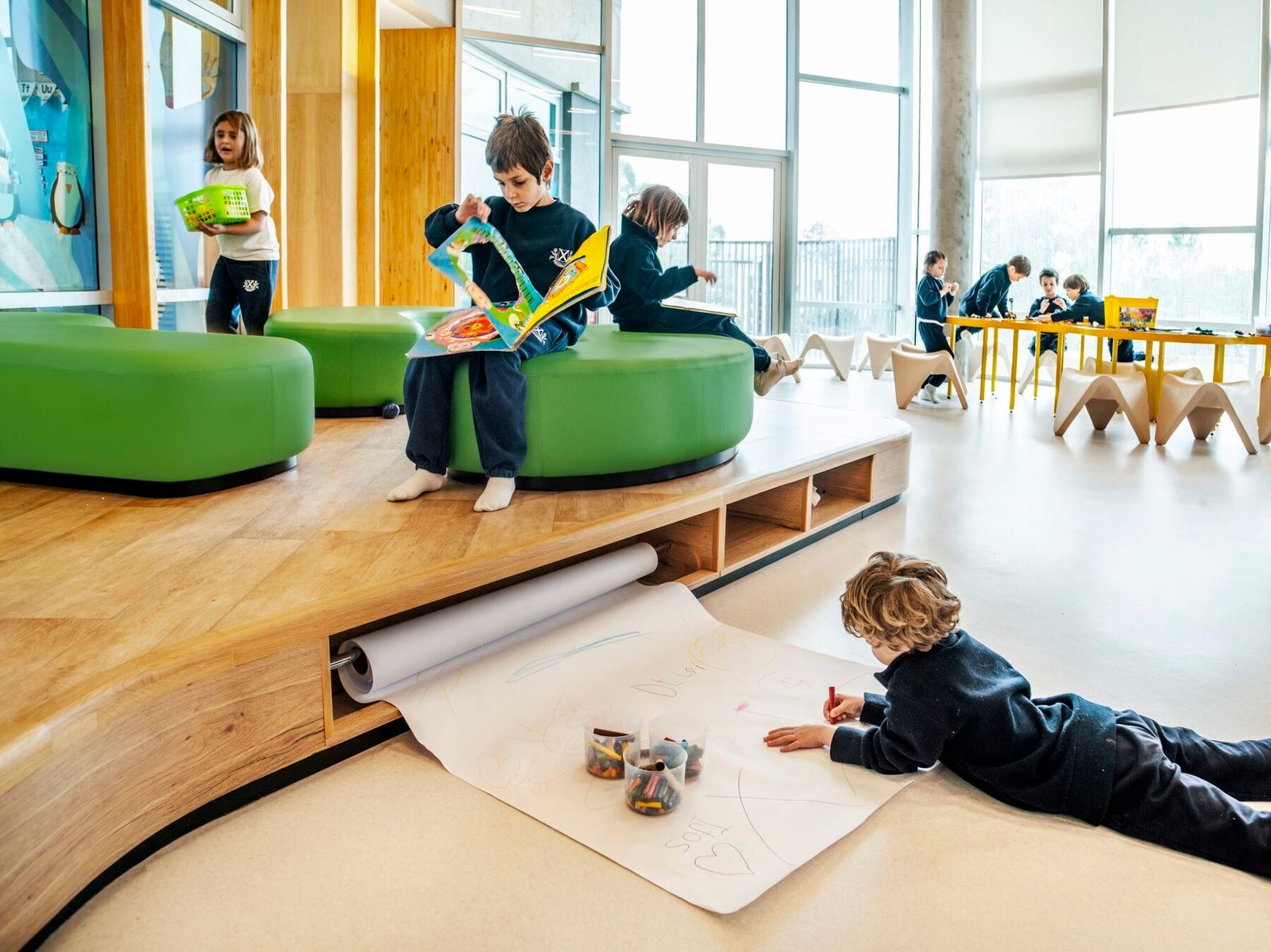 modern-kindergarten-window-seating საბავშვო ბაღის ინტერიერი გეომეტრიული ფანჯრის რაფებით და სათამაშო ზონებით.
