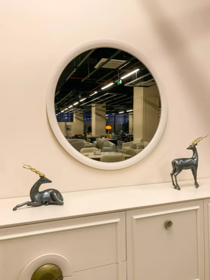 კედლის დეკორი, მრგვალი სარკე და ავეჯის კომპოზიცია თანამედროვე შოურუმის ინტერიერში.